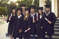 Graduate students in robes and caps holding diplomas near university campus. Young people celebrating commencement Royalty Free Stock Photo