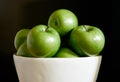 A group of green Granny Smith apples in a white fruit bowl against a dark brown background. Royalty Free Stock Photo