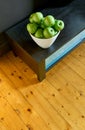 A group of green Granny Smith cooking apples in a white bowl on a brown wooden bench  and a vibrant wooden floor from above. Royalty Free Stock Photo