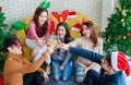 Group of happy Asian male female friends wear Santa Claus hat and reindeer antler headband cheers champagne glasses together