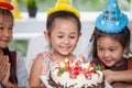 group of happy children girl with hat blowing candles on  birthday cake together celebrating in party . adorable kids gathered Royalty Free Stock Photo