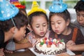 group of happy  children with hat blowing candles on  birthday cake together celebrating in party . adorable kids gathered around Royalty Free Stock Photo