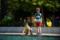 Group of happy children playing outdoors near pool or fountain. Kids having fun in park during summer vacation. Dressed in Royalty Free Stock Photo