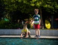 Group of happy children playing outdoors near pool or fountain. Kids having fun in park during summer vacation. Dressed in Royalty Free Stock Photo