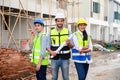 Group of happy contractors, engineers and formats in safety vests with helmets stand on the under-construction building site. Royalty Free Stock Photo