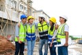 Group of happy contractors, engineers and formats in safety vests with helmets stand on the under-construction building site. Royalty Free Stock Photo