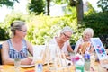 Group of happy elderly women attending an outdoor art class in a garden or park painting from sample pictures on easels while