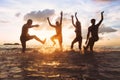 Group of happy friends or family having fun together on the beach at sunset, jumping and dancing