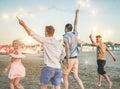 Group of happy friends running on the beach with fireworks sparklers - Young people having fun doing party in summer holidays - Royalty Free Stock Photo