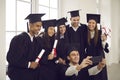 Group of happy international students with diplomas taking selfie using smartphone in classroom. Royalty Free Stock Photo