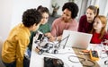 Happy kids with their African American female science teacher with laptop programming electric toys and robots at robotics