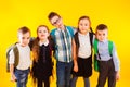 Group of happy kids in uniform with school bags hugging and looking to camera over yellow background Royalty Free Stock Photo