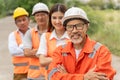 Group of happy 3 males and 1 female engineers wearing orange jumpsuit, hardhat and safety vest smiling and standing outside with