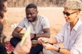 Group of happy multiracial friends having fun together on the beach, playing cards on picnic, laughing. Mixed race people Royalty Free Stock Photo