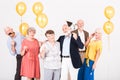 Happy senior friends holding yellow balloons and standing in white interior