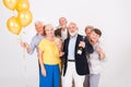 Happy senior friends holding yellow balloons and standing in white interior