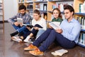Group of happy students studying together in library, sitting on floor on background with bookshelves Royalty Free Stock Photo