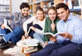 Group of happy students studying together in library, sitting on floor on background with bookshelves Royalty Free Stock Photo