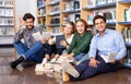 Group of happy students studying together in library, sitting on floor on background with bookshelves Royalty Free Stock Photo