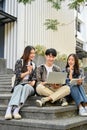 Group of happy young Asian college students sitting on stairs in front of the campus building Royalty Free Stock Photo