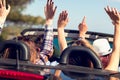 Group of happy young friends in cabriolet with raised hands driving on sunset Royalty Free Stock Photo