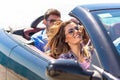 Group of happy young friends in cabriolet with raised hands driving on sunset Royalty Free Stock Photo