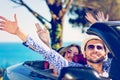 Group of happy young friends in cabriolet with raised hands driving on sunset Royalty Free Stock Photo