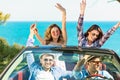 Group of happy young friends in cabriolet with raised hands driving on sunset Royalty Free Stock Photo