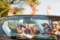 Group of happy young friends in cabriolet with raised hands driving on sunset Royalty Free Stock Photo