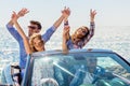 Group of happy young friends in cabriolet with raised hands driving on sunset Royalty Free Stock Photo