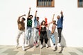 Group of happy young friends having fun and laughing, jumping over white wall. Diverse millennial people spending time together.