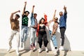 Group of happy young friends having fun and laughing, jumping over white wall. Diverse millennial people spending time together.