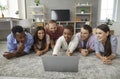 Group of happy young friends lying on floor at home and watching movie on laptop Royalty Free Stock Photo