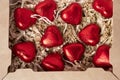 A group of heart-shaped chocolates wrapped in red foil, lying in a gift box.