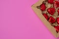 A group of heart-shaped chocolates wrapped in red foil, lying in a gift box on a pink background