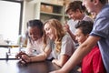 Group Of High School Students Looking At Message On Mobile Phone In Classroom