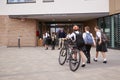 Group Of High School Students Wearing Uniform Arriving At School Walking Or Riding Bikes Being Greeted By Teacher Royalty Free Stock Photo
