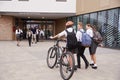 Group Of High School Students Wearing Uniform Arriving At School Walking Or Riding Bikes Being Greeted By Teacher Royalty Free Stock Photo