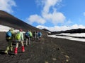 A group of hikers on black ash next to a lava field and snow in in Kamchatka, Russia