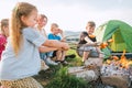Group of Kids - Boys and girls cheerfully smiling and roasting sausages on sticks over a campfire flame near the green tent. Royalty Free Stock Photo