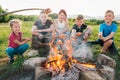 Group of Kids - Boys and girls cheerfully smiling and roasting sausages on sticks over a campfire flame Sausages selective focus. Royalty Free Stock Photo