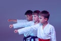Group of kids, different boys, taekwondo athletes in white doboks in action on lilac color background. Concept