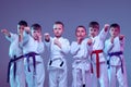 Group of kids, different boys, taekwondo athletes in white doboks in action isolated on lilac color background. Concept