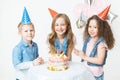 Group of kids in festive cap sit near birthday cake and smile. Celebration. Birthday party. Balloons on the background Royalty Free Stock Photo