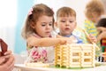 Group of kids playing in kindergarten. Children building toy house with blocks sitting together by the table Royalty Free Stock Photo