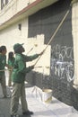 A group of kids repainting the side of a building defaced by graffiti