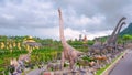 Group of large dinosaur statues and topiary garden with tourists walking on walkway in tropical valley at Nong Nooch garden