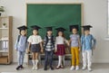 Group of little school kids in graduation caps standing in classroom and holding hands Royalty Free Stock Photo