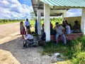 A group of locals and one tourist waiting at a remote bus stop for the local bus heading to Placencia along the side of the highwa