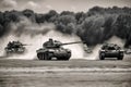 Group of main battle tanks with a city on fire on the background. One tank firing a shell from the barrel. Military or